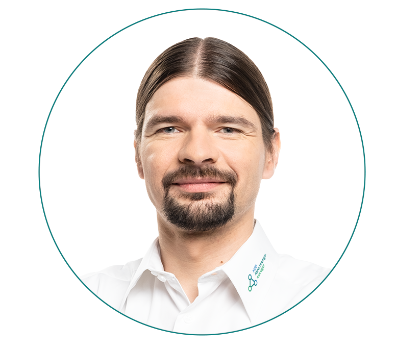 Porträt von Ralf Schwarzmaier mit langen Haaren und Bart, in einem weißen Hemd.